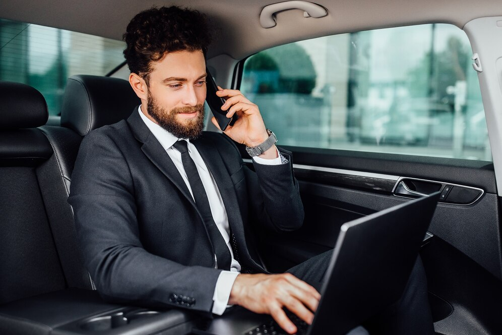 Picture of a business man sitting in the backseat of his car using his computer.